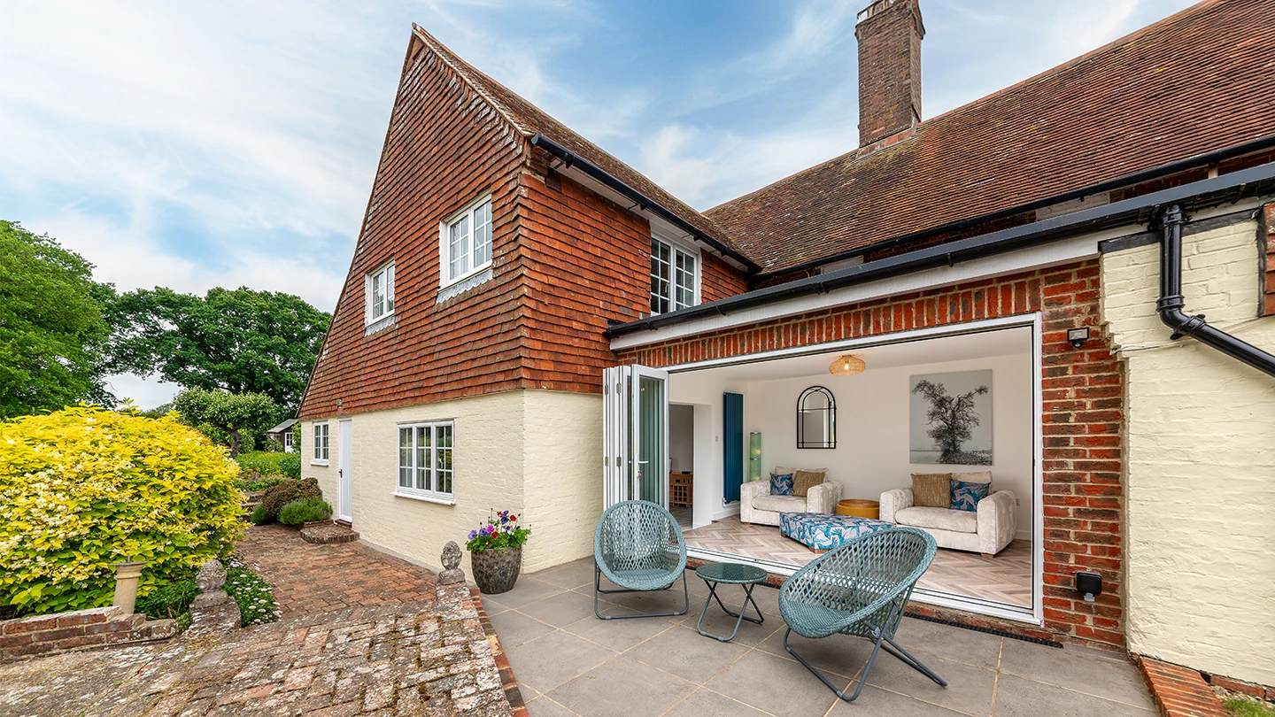 Traditional cottage with bifold doors opening onto a patio seating area and landscaped garden